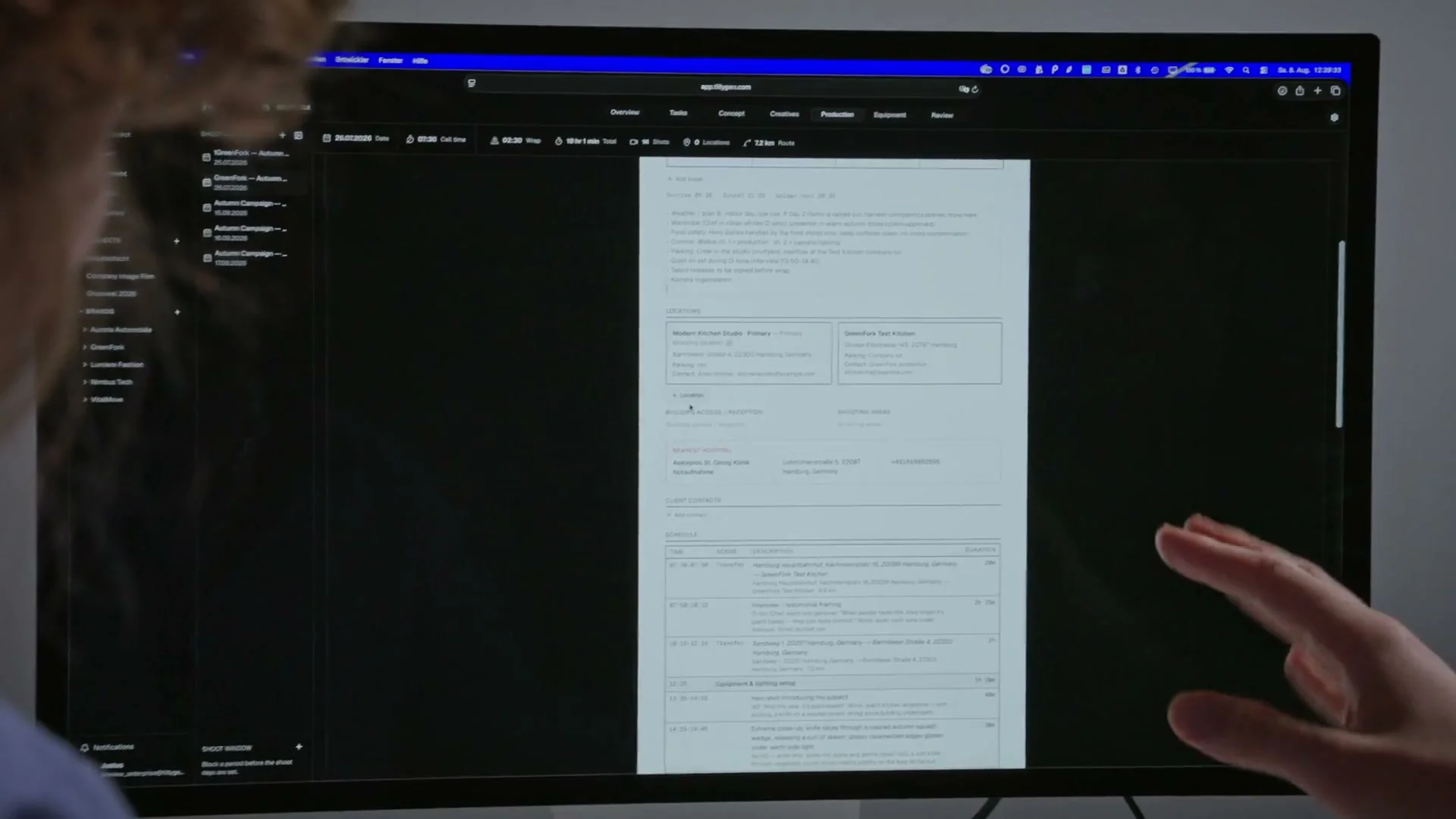 A hand pointing at a call sheet in TillyBoard on a large monitor, with locations, the nearest hospital and the schedule.