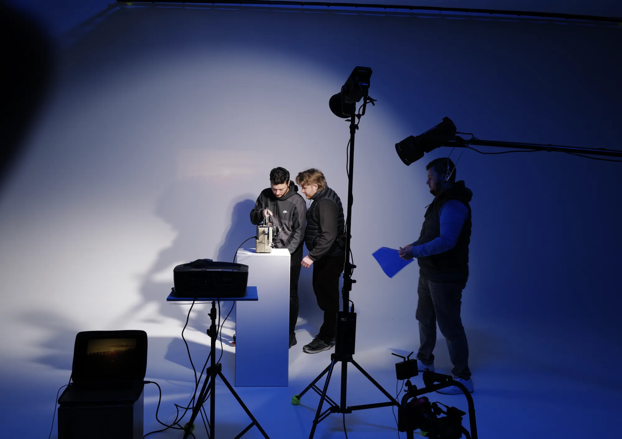 Drei aus dem Team richten im blau ausgeleuchteten Studio eine Projektor-Einstellung ein