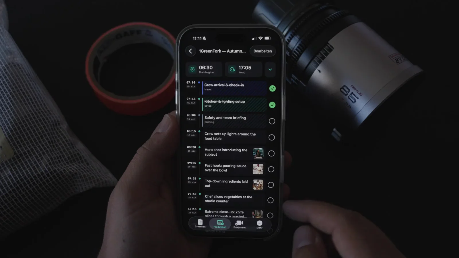 A hand holding an iPhone with the TillyBoard day plan for the GreenFork autumn campaign: call 06:30, wrap 17:05, the first two blocks ticked green.